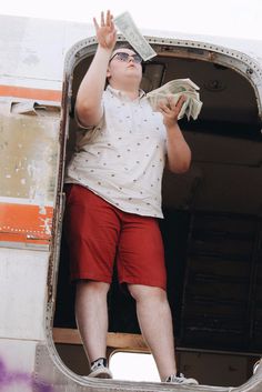 a man in red shorts and white shirt holding money while standing inside an airplane door