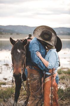 a man and woman hugging each other while standing next to a horse in a field