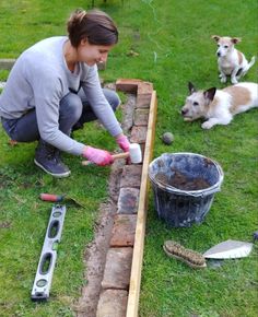 a woman kneeling down next to a brick wall with two dogs on the other side