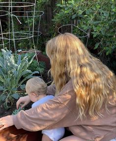 a woman kneeling down next to a little boy in front of a garden filled with plants