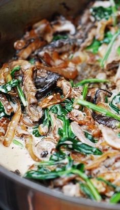 a pan filled with mushrooms and greens on top of a stove