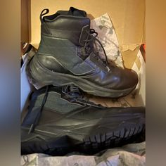 two pairs of black hiking boots sitting on top of a cardboard box next to each other