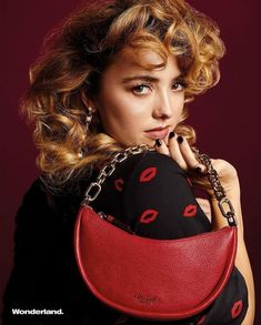 a woman holding a red purse with chains around her neck and looking at the camera