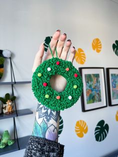 a person holding up a green wreath with candy on it in front of a wall