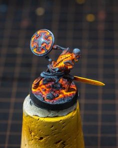 a toy figurine is sitting on top of a yellow and black pole with flames