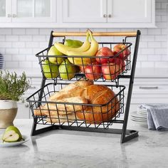 a wire basket filled with fresh fruit and bread on top of a kitchen counter next to a potted plant