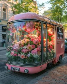 a pink bus with flowers on the front and side is parked next to a sidewalk