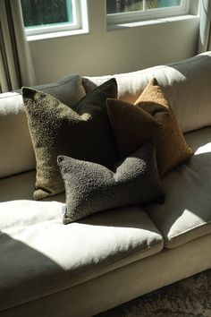 three pillows are sitting on a couch in front of two windows with sunlight streaming through them