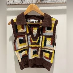 a brown and yellow sweater hanging on a white wall next to a wooden hanger