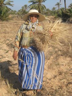 a man in a straw hat is carrying a blue and white striped bag with palm trees in the background