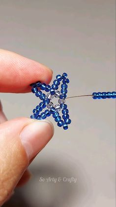 someone is making a beaded snowflake ornament out of blue seed beads