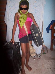 a woman standing in a room with luggage and a scarf around her neck, holding two pieces of luggage