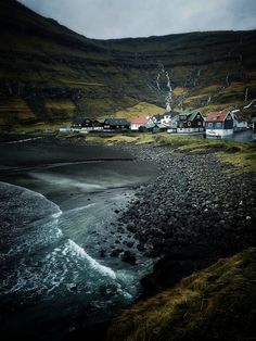 a small village on the side of a hill next to a body of water with waves coming in