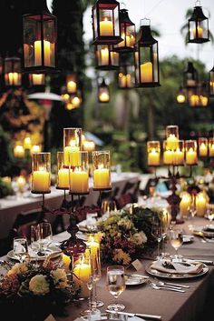 a long table with many lit candles and place settings for dinner guests to sit at