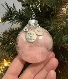 a hand holding a pink ornament with two baby's first christmas tags