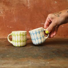 two coffee mugs sitting on top of a table next to each other, one holding a green and white polka dot cup