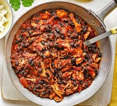 a skillet filled with beans and meat on top of a cutting board next to rice