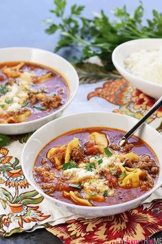 two bowls of pasta and meat soup on a colorful place mat with parmesan cheese