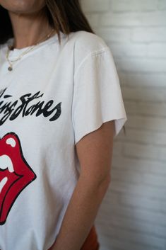 a woman wearing a rolling stones t - shirt standing in front of a brick wall