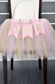 a pink and gold first birthday party chair with one banner on it's back