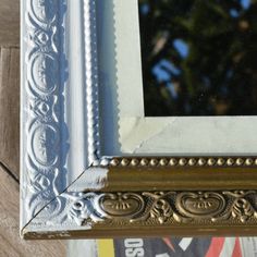 an ornate gold and silver frame hanging on a wall with a tree in the background