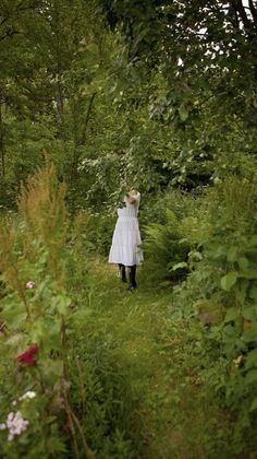 a woman in a white dress walking through the woods