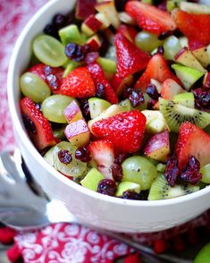 a white bowl filled with fruit salad on top of a red and white table cloth