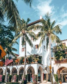 palm trees line the street in front of a white building with an american flag hanging from it's roof