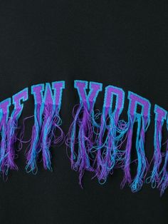 two purple and blue letters that spell new york on a black background with long strands of yarn