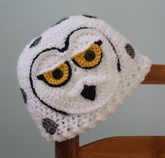 a white crocheted hat with black and yellow eyes on top of a wooden chair