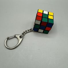 a rubik cube keychain is shown on a gray surface with a metal hook