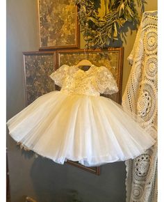 a white dress hanging on a rack in front of a wall with lace and crochet