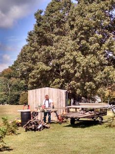 a man standing in front of a wooden outhouse on top of a lush green field