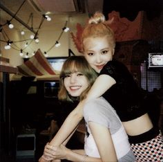 two young women hugging each other in a room with lights on the wall behind them