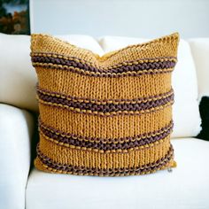 a yellow and brown knitted pillow sitting on top of a white couch next to a black cat