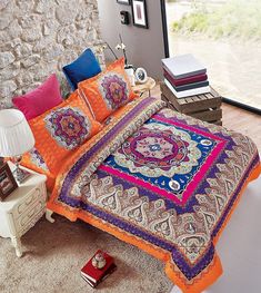 a bed with an orange and blue comforter on top of it next to a window