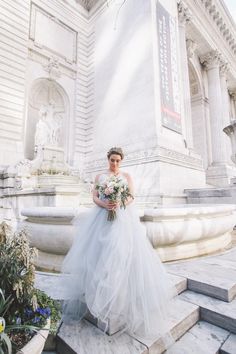 a woman in a wedding dress is standing on some steps near a fountain with flowers