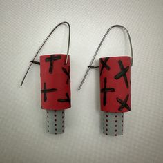 two pairs of earrings made out of toilet paper with crosses painted on them, hanging from hooks