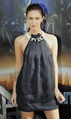 a woman standing in front of a movie poster wearing a black dress and silver necklace