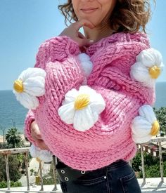 a woman is wearing a pink sweater with white flowers on it and posing for the camera