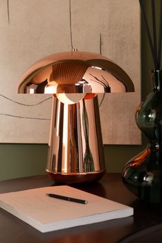 a desk lamp sitting on top of a wooden table next to a pen and paper