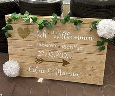 a wooden sign sitting on top of a sidewalk next to some white flowers and green leaves