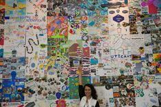 a woman standing in front of a wall covered with pictures and stickers on it