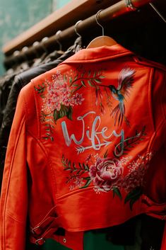 an orange jacket with the words wife written on it hanging from a rack in a store