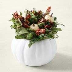 a white pumpkin filled with greenery and pine cones