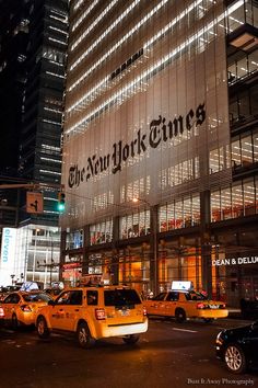 the new york times building is lit up at night with taxi cabs parked in front