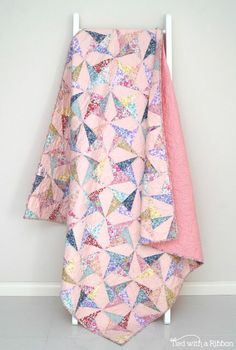 a pink and blue quilt hanging on the wall next to a white rack with two folded towels