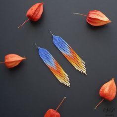 two pairs of beaded earrings with orange and blue beads next to each other on a black surface