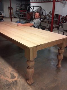 a man sitting at a wooden table in a garage with his hand on the top