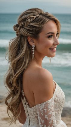 a woman with long hair wearing a wedding dress on the beach, looking off to the side